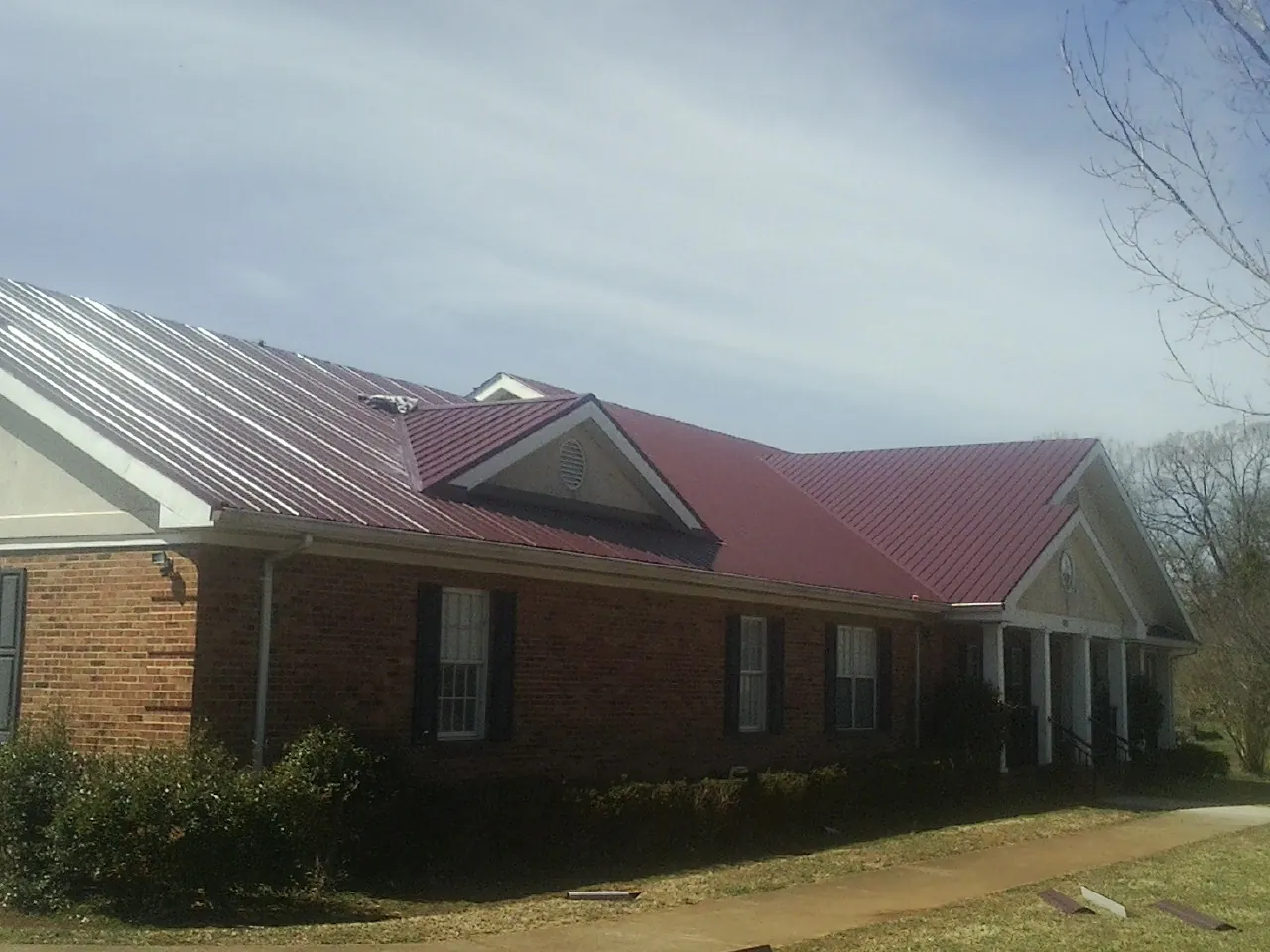 Red metal roof with gabled entries on a long brick building, from a Hail Damage Roof Repair job in Stow