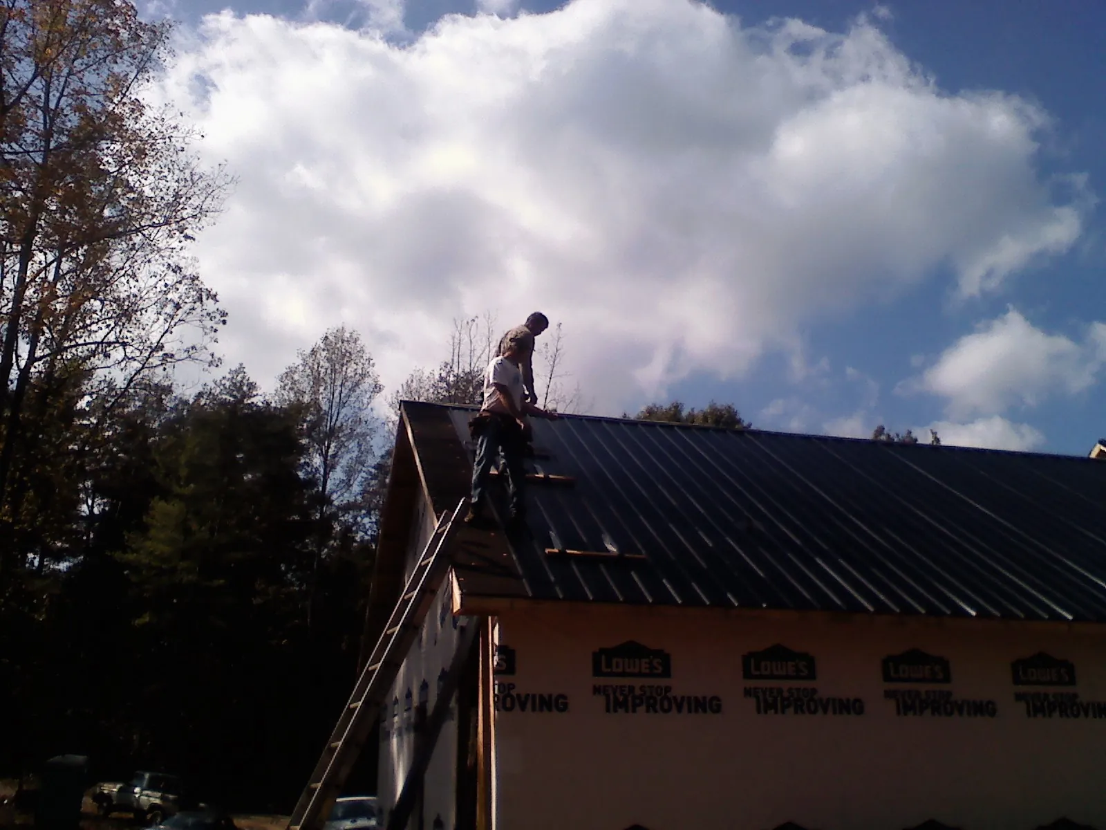 Roofer fastening dark metal panels high against a cloudy sky, from a Roof Inspection job in Stow