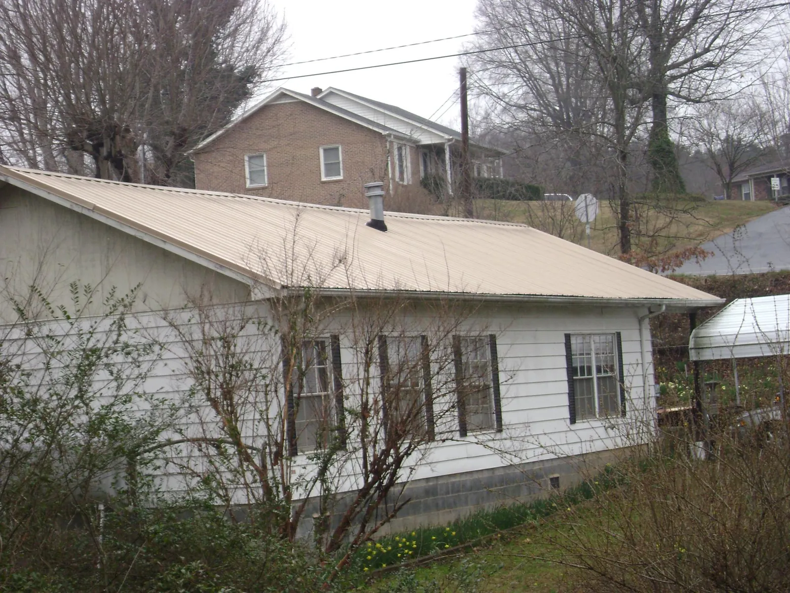 Tan metal roof on a white sided house set into a hillside — Commercial Roofing by Roofing Brothers in Stow